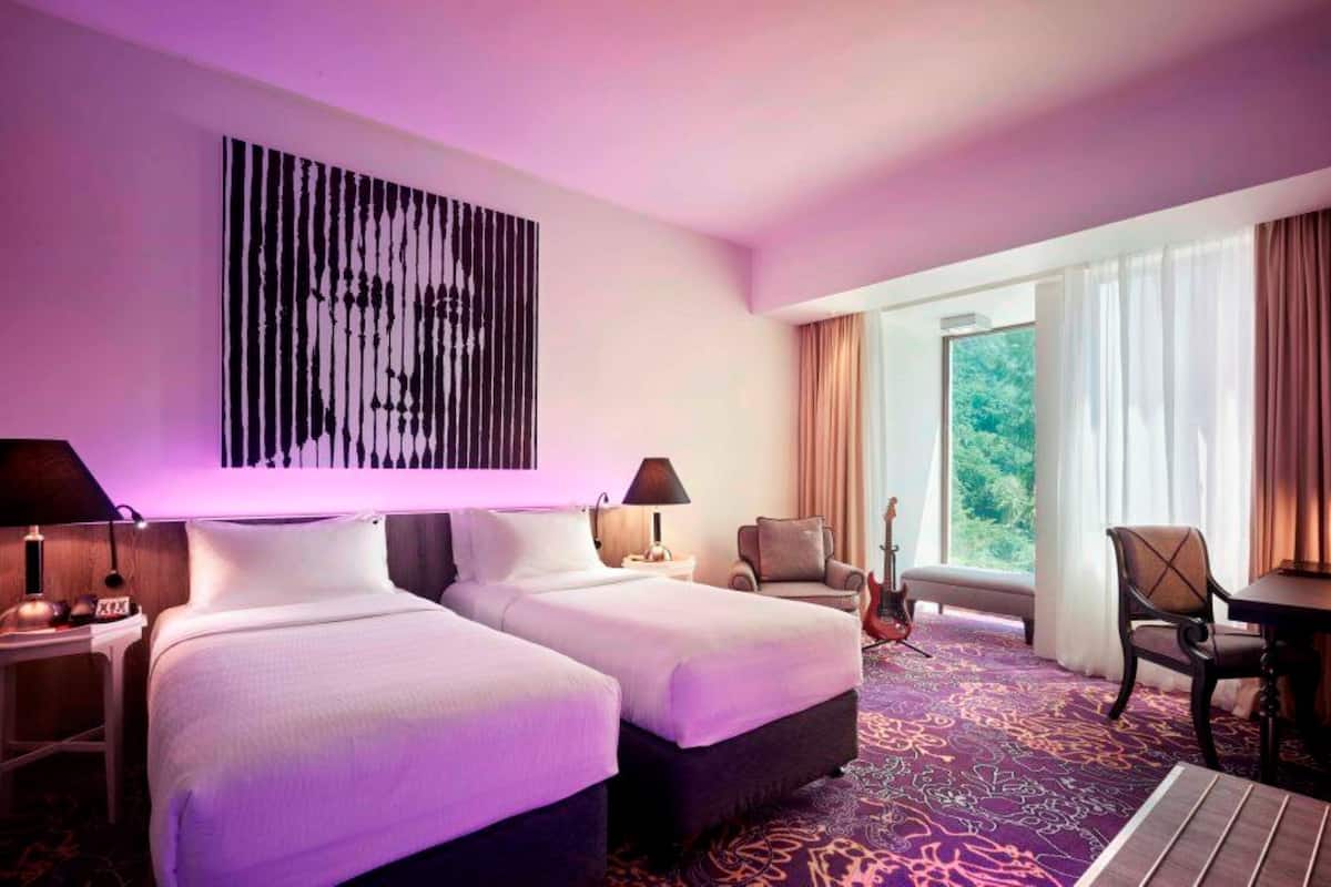 A hotel room with two beds, a desk, a chair, a guitar, and a large window with curtains.