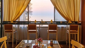 Un coin repas avec une table dressée pour quatre personnes, une vue sur la mer grâce à de grandes fenêtres et un balcon agrémenté d’une balustrade.