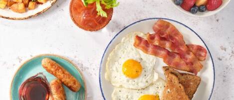 Prato de café da manhã com ovos, bacon, torradas, salsichas e uma cesta de frutas.