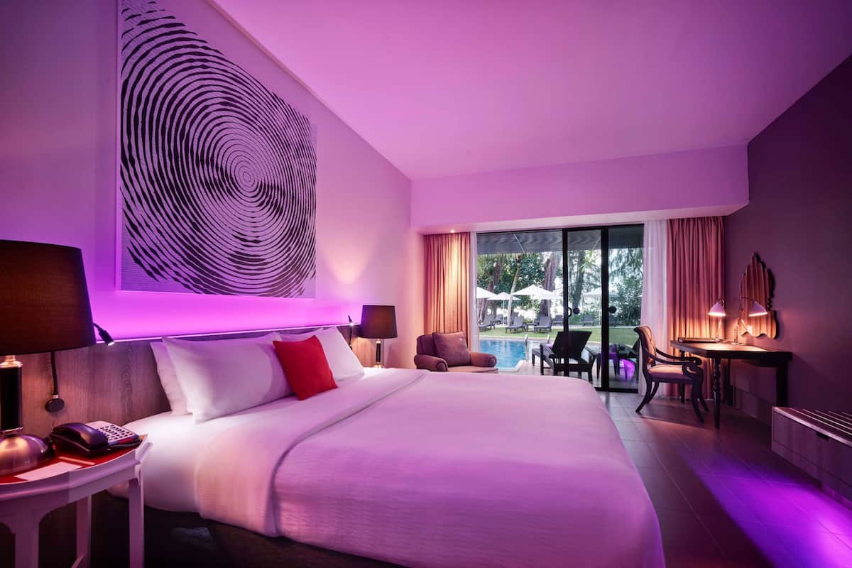 A hotel room with a large bed, a desk, a chair, and a view of an outdoor pool area.