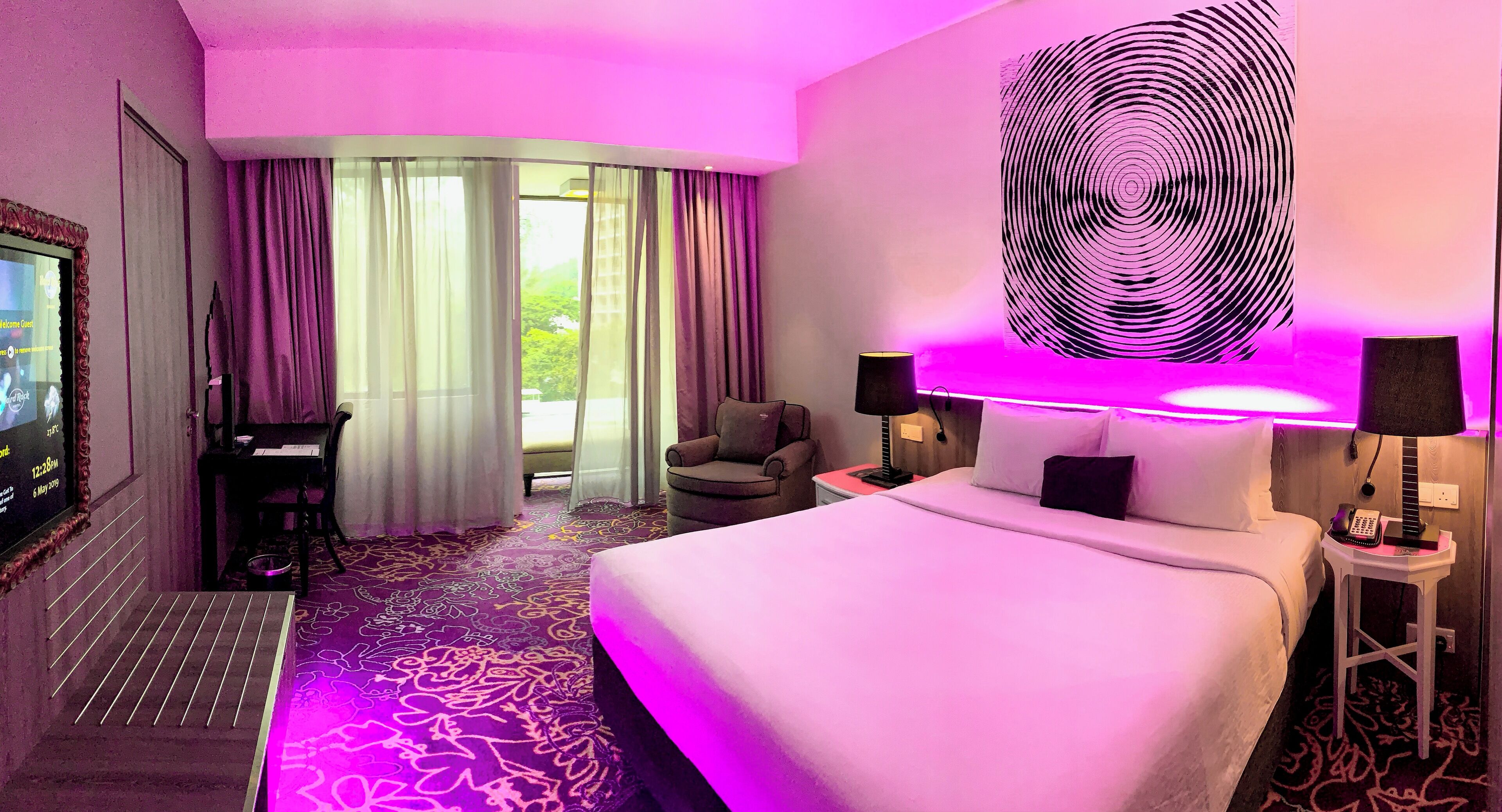 Habitación de hotel con una cama grande, un escritorio con una silla, un televisor y vistas a zonas verdes.