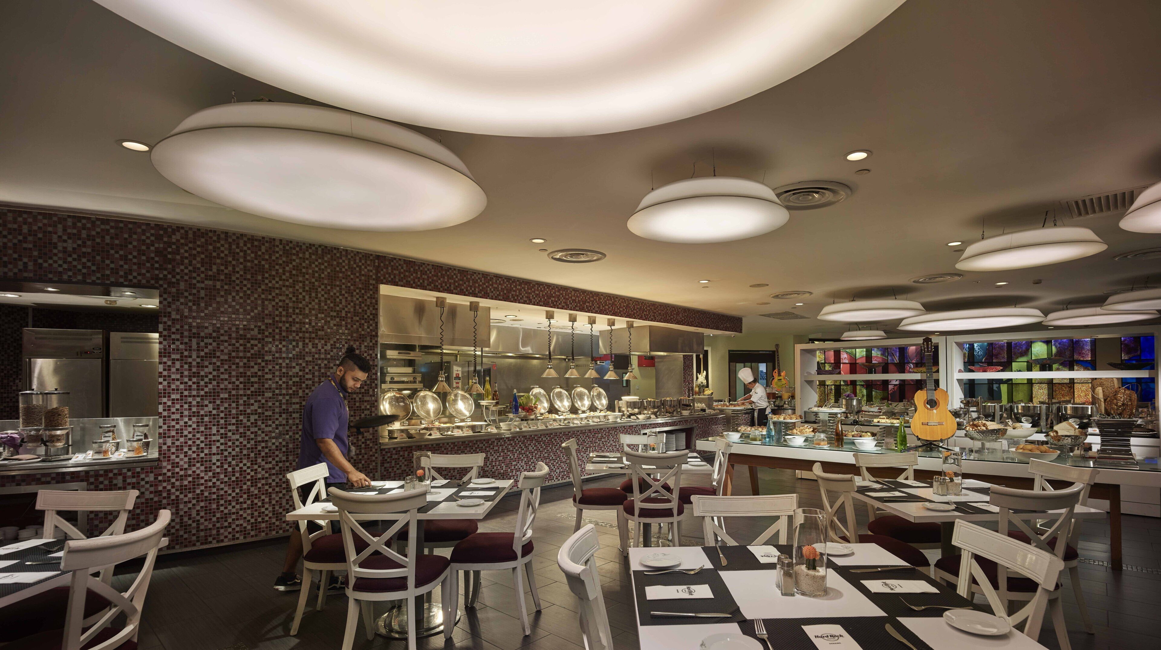 A modern restaurant with a central bar area, white chairs, and a variety of dishes displayed.