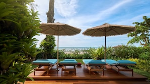 Une terrasse en bois avec des chaises longues et des parasols en chaume, donnant sur une plage.