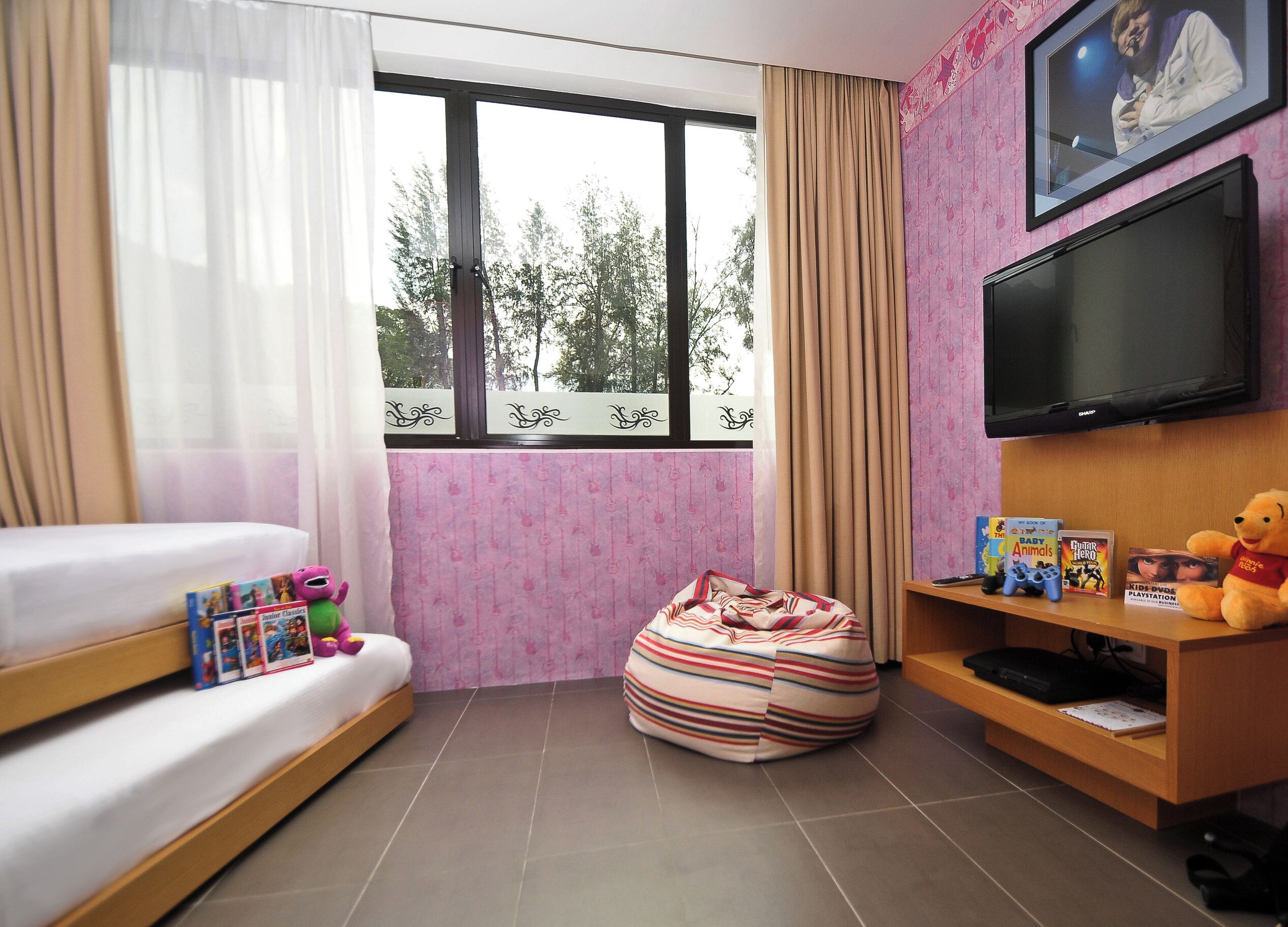 Een hotelkamer met een bed, een relaxfauteuil, een televisie en kinderboeken.