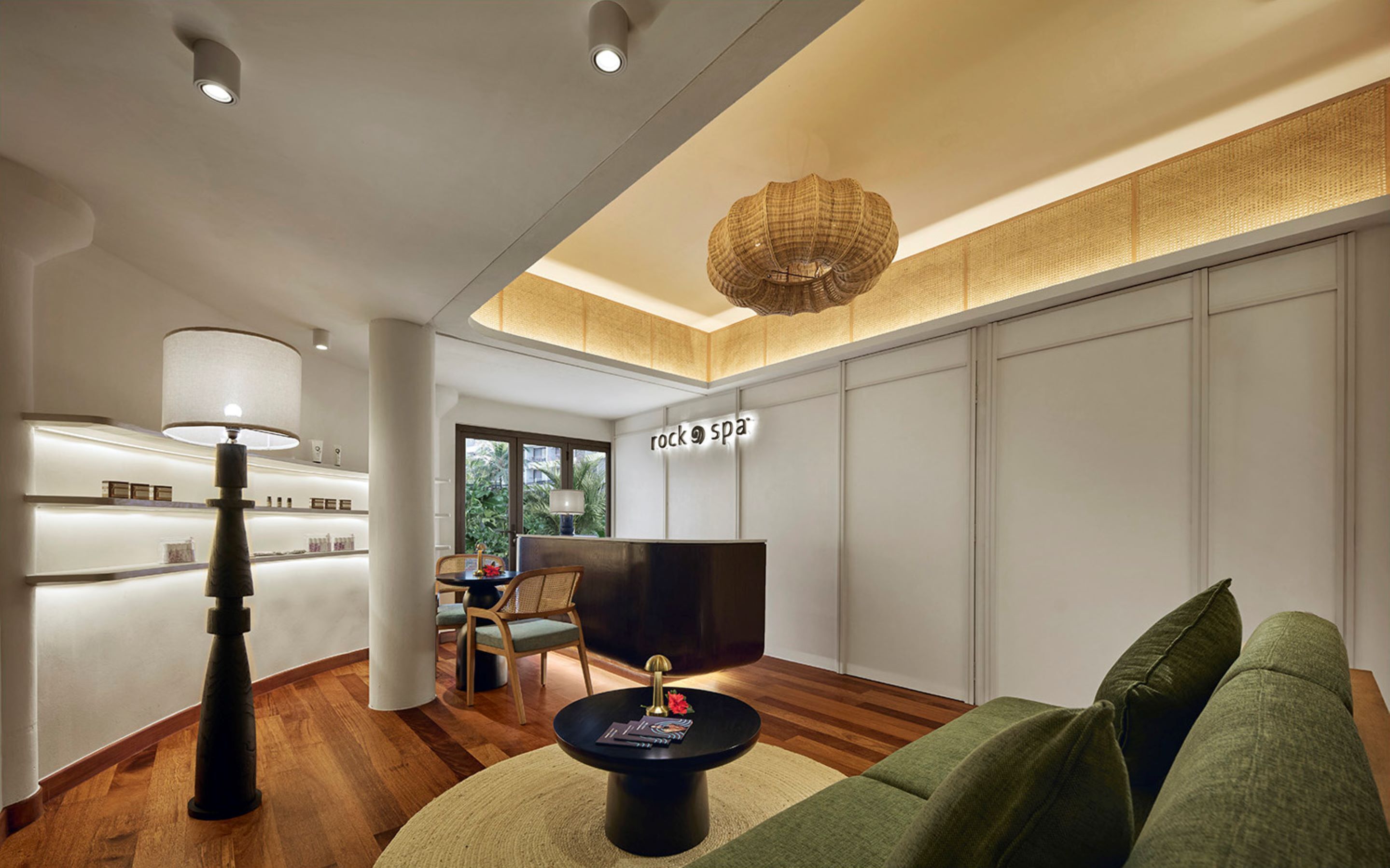 A modern living room with a sofa, a coffee table, a TV, and a lamp. There is a reception desk with a sign that reads "rock spa".