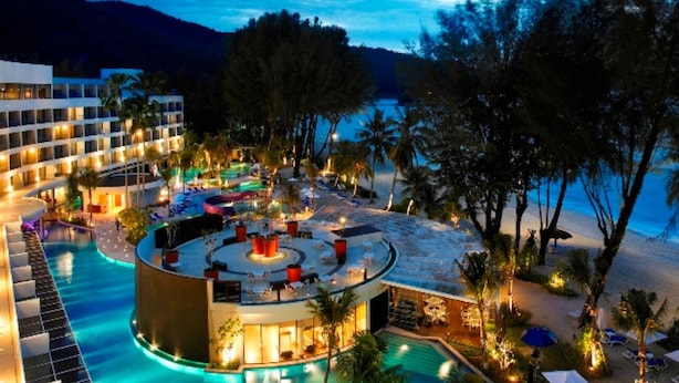 Un espace piscine aménagé dans un complexe hôtelier, avec un bar circulaire, des chaises longues et une vue sur la plage et les montagnes.