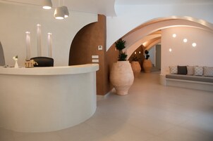 Un área de recepción moderna con un mostrador curvo, jarrones grandes y una zona de estar con cojines.