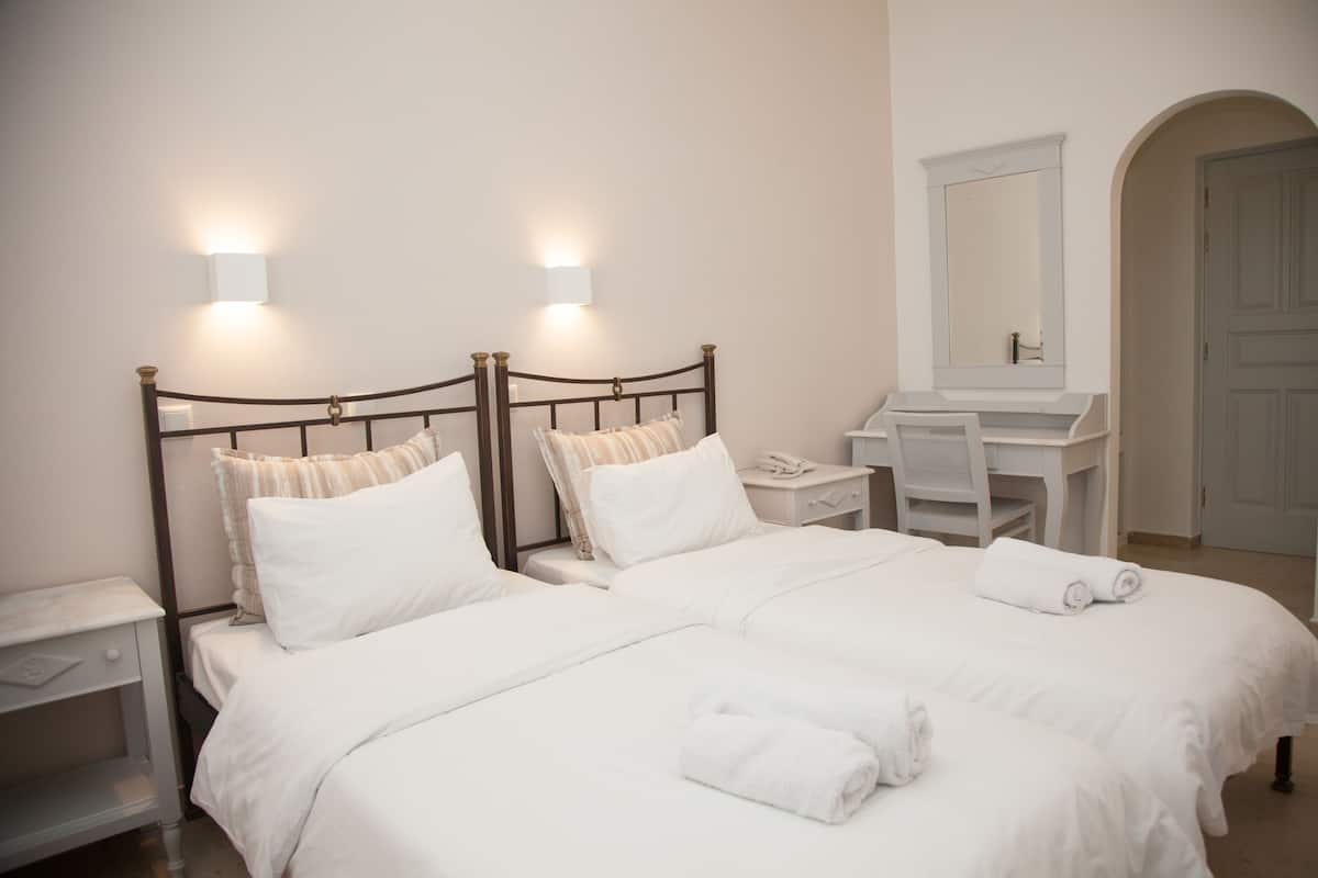 A hotel room with a double bed, bedside tables, a desk, a mirror, and a bathroom vanity.