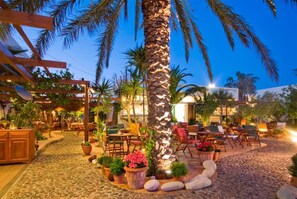 An outdoor patio area with stone flooring, wooden furniture, and potted plants. - Pelican Hotel (Santorini)