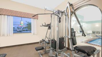 A gym with exercise equipment, a window with curtains, and a pool area visible through the window.