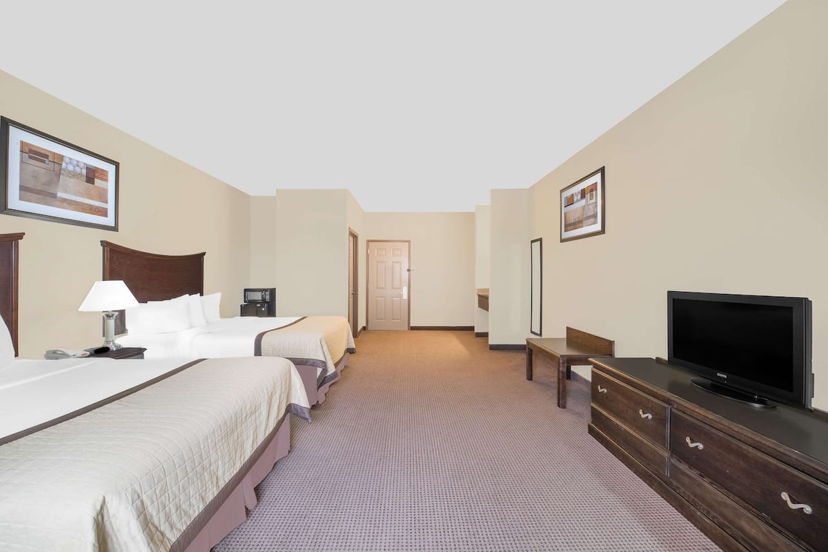 Een hotelkamer met twee bedden, een televisie, een dressoir en een deur die naar een andere kamer leidt.
