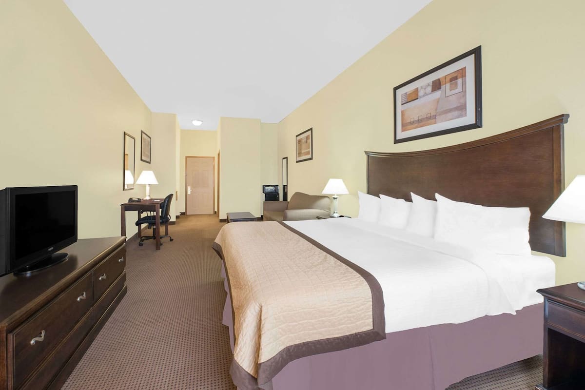 Een hotelkamer met een groot bed, een televisie, een bureau met een stoel, en een deur naar een andere kamer.