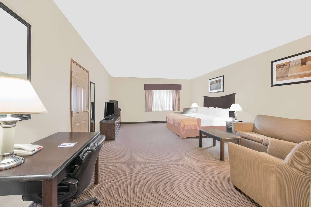 Een hotelkamer met een bed, een slaapbank, een bureau met lamp, een televisie en een raam met gordijnen.