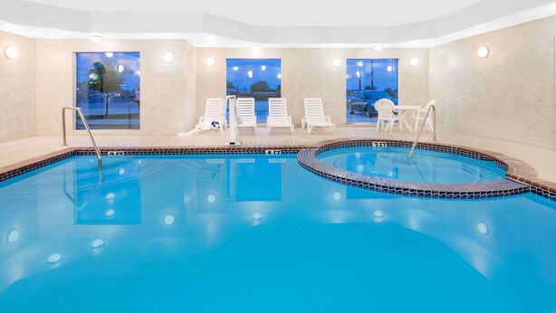 A swimming pool with a tiled edge, a sun lounger area, and a view through large windows. - Baymont by Wyndham Snyder (Snyder)