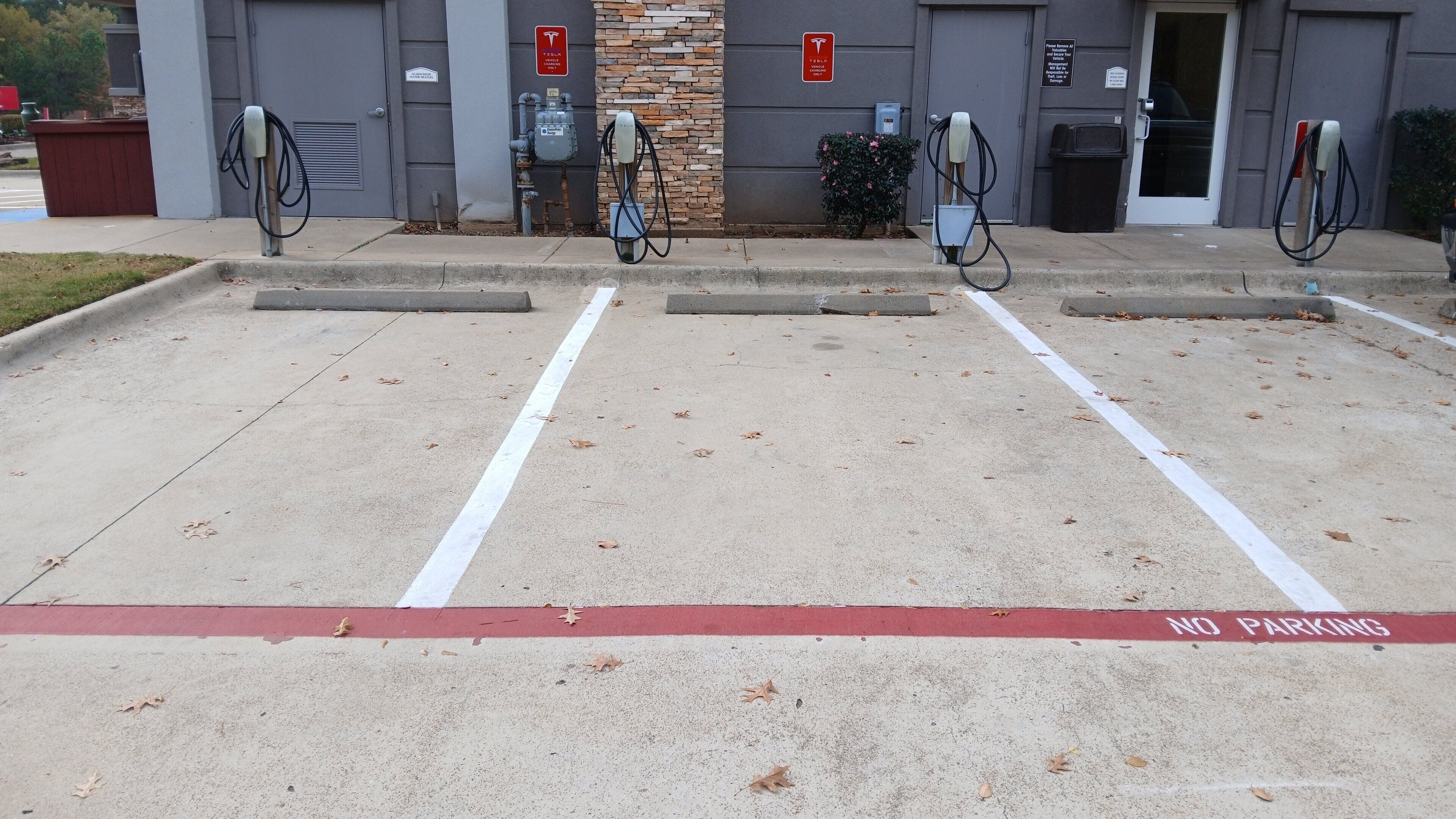 A parking area with electric vehicle charging stations, a no parking sign, and a building entrance.