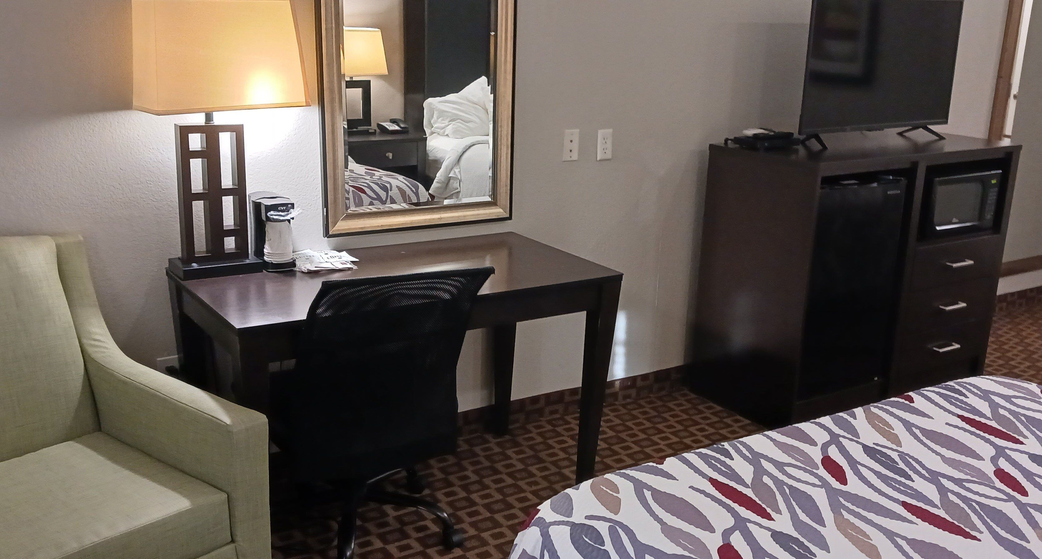 Une chambre d’hôtel comprenant un lit, un bureau avec une chaise, une commode, un miroir et une lampe.