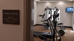 Ein Fitnessstudio mit Trainingsgeräten, einem Fernsehbildschirm und einer Schanze mit Öffnungszeiten.