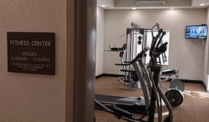 A fitness center with exercise equipment, a television screen, and a sign indicating hours of operation. - Red Roof Inn & Suites Longview (Longview)