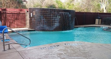 Una piscina con una cascada, una valla de madera y una silla azul.