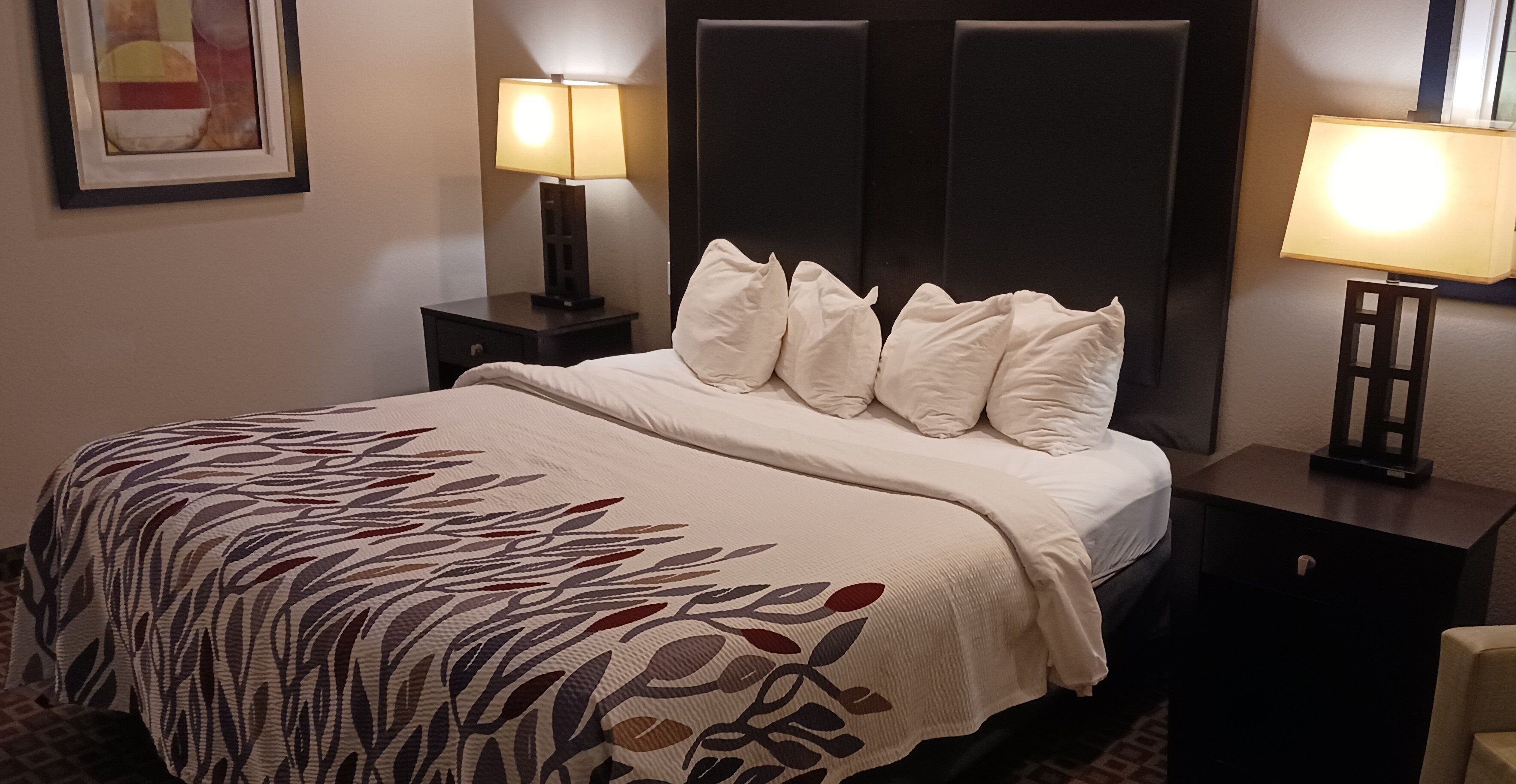 Habitación de hotel con cama, dos lámparas de noche, una mesita de noche y un cuadro en la pared.