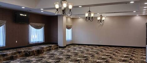 Sala de conferências com carpete estampado, várias lustres e grandes janelas com cortinas.