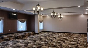 A conference room with patterned carpet, multiple chandeliers, and large windows with curtains.