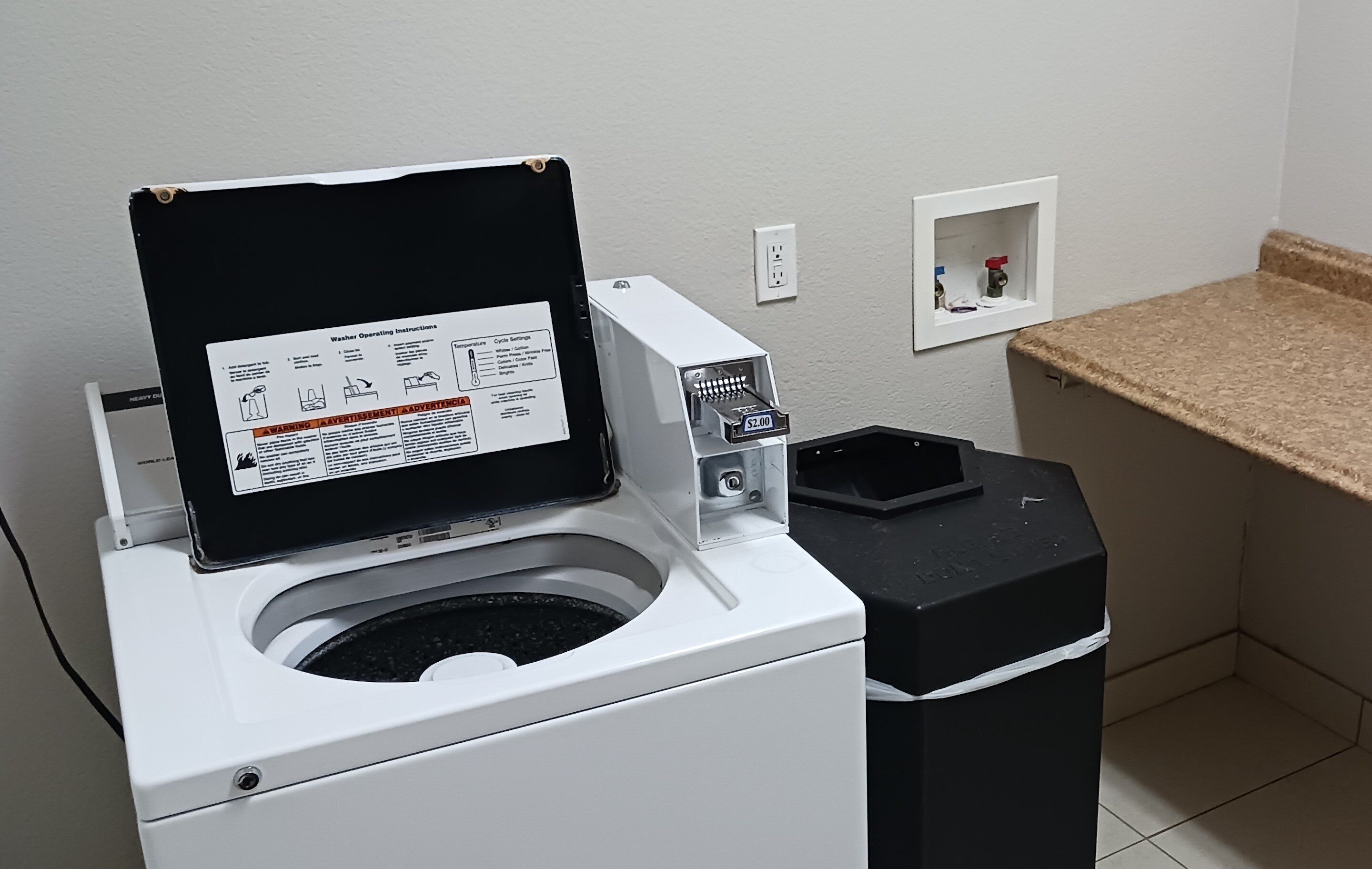 A front-loading washing machine with a control panel and a coin slot for payment.