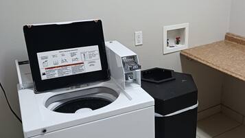 A front-loading washing machine with a control panel and a coin slot for payment.