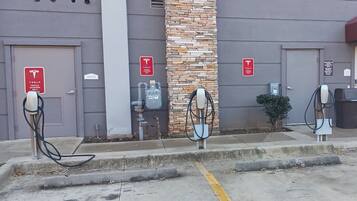 A parking area with three Tesla charging stations, a water heater, and a building with a stone facade.