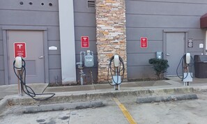 A parking area with three Tesla charging stations, a water heater, and a building with a stone facade. - Red Roof Inn & Suites Longview (Longview)