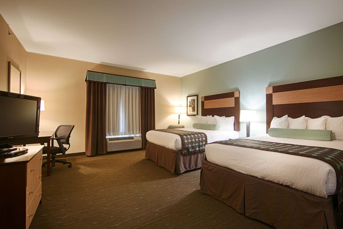 A hotel room with two beds, a desk with a television, and a chair.