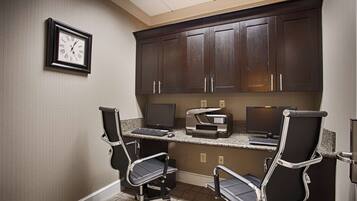 A small office space with two desks, two chairs, a framed clock, and dark wooden cabinets.