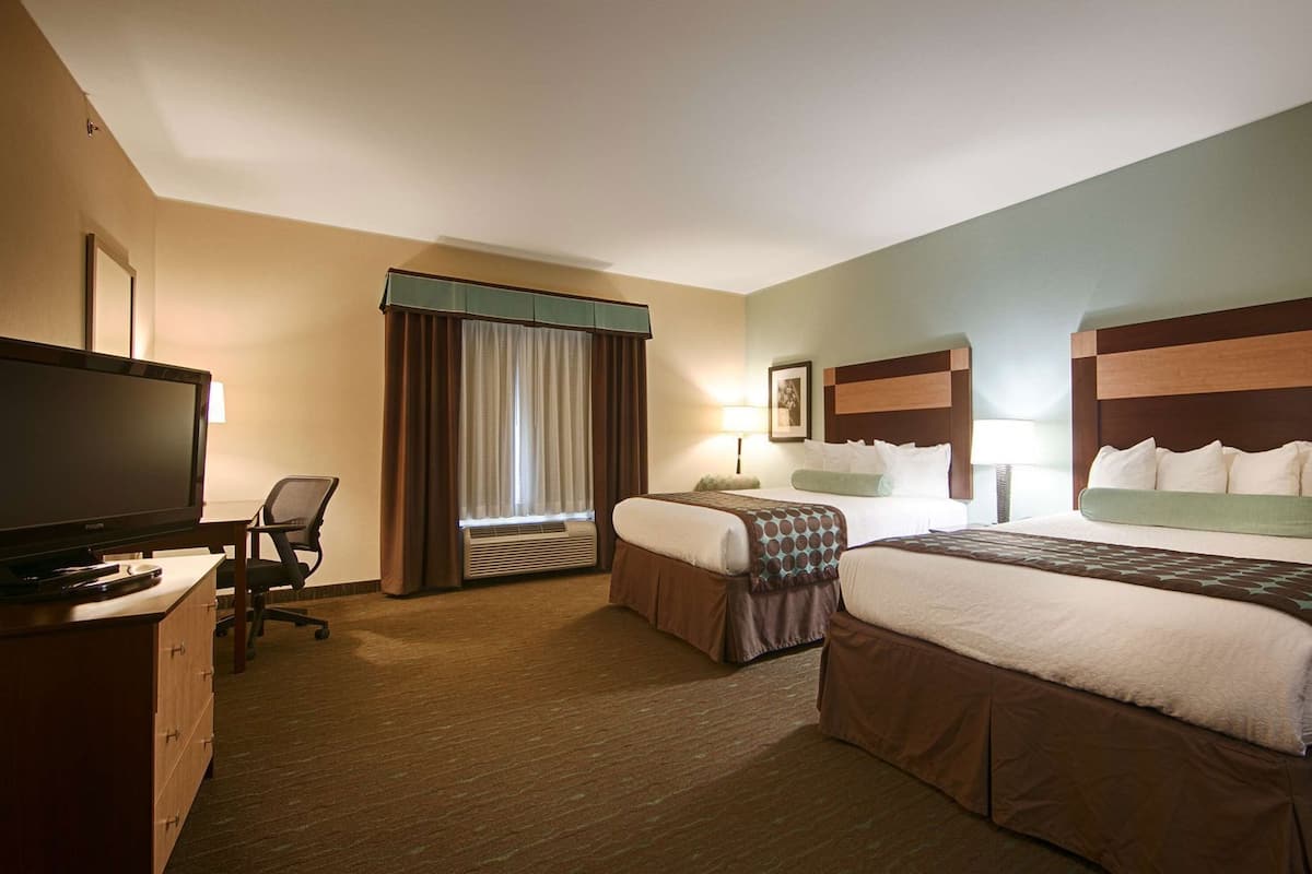 A hotel room with two beds, a TV, a desk, and a chair.