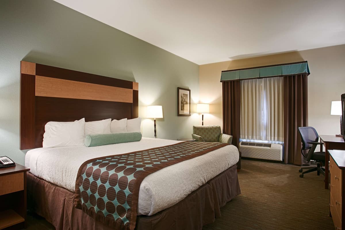 A hotel room with a large bed, bedside lamps, a desk with a television, and a chair.