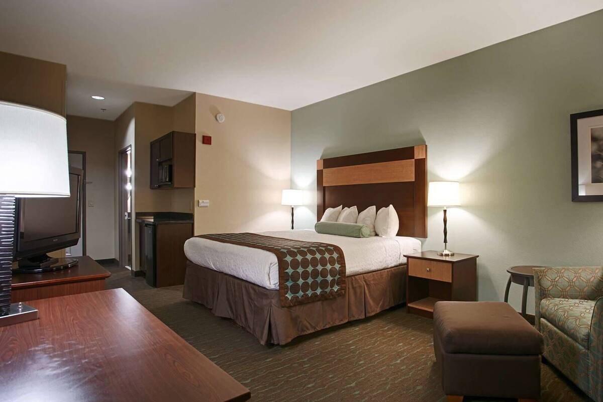 A hotel room with a bed, bedside lamps, a desk, a chair, and a television.