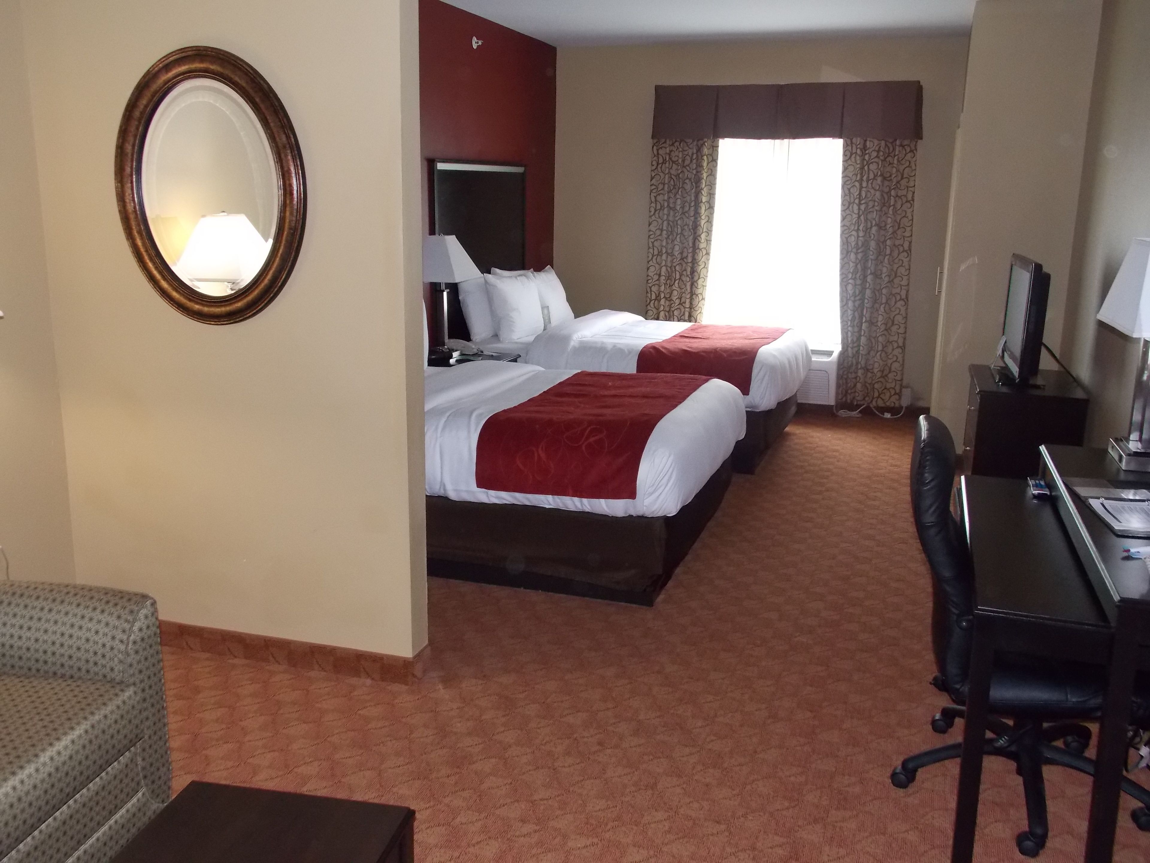 A hotel room with two beds, a desk, a chair, a TV, and a mirror.