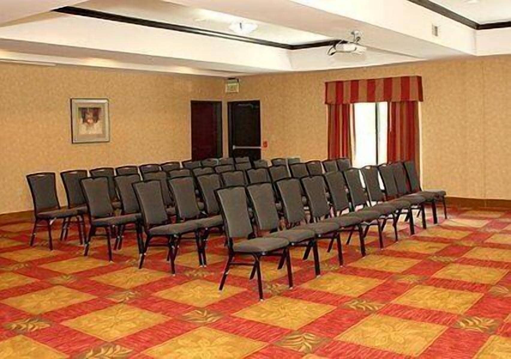 Un salón de conferencias con hileras de sillas, piso alfombrado y una pantalla de proyector.