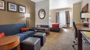 Una habitación de hotel con un sofá azul, un escritorio de madera, una cama con manta roja, un espejo y cuadros enmarcados en la pared.