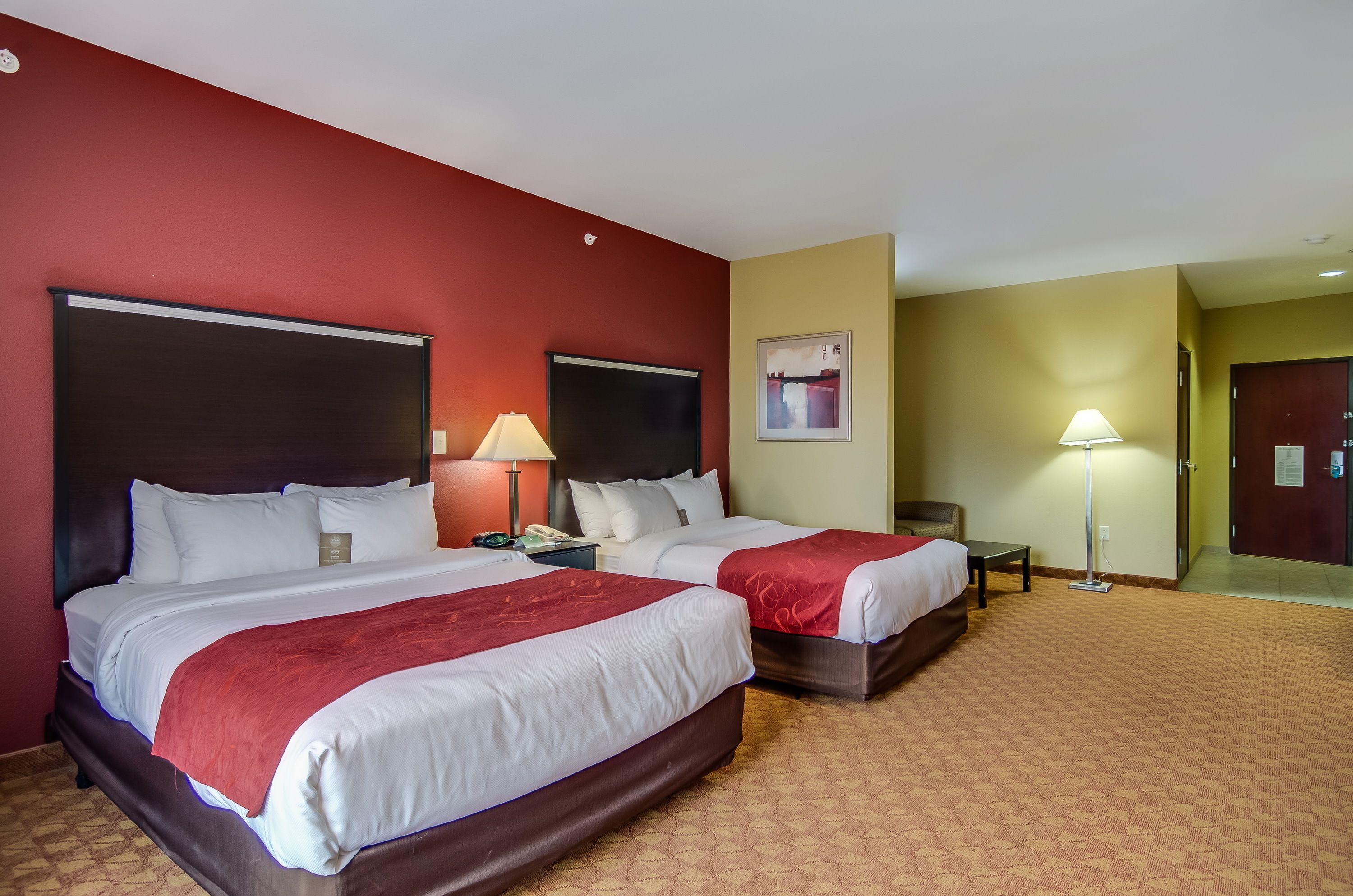 Een hotelkamer met twee bedden, een bureau, een stoel, een lamp en een schilderij aan de muur.