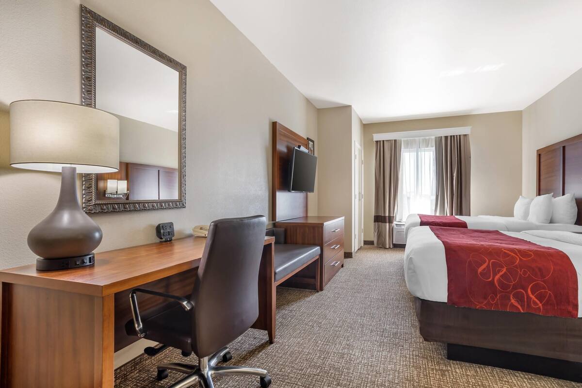 A hotel room with a desk, chair, TV, and a bed with a red blanket.