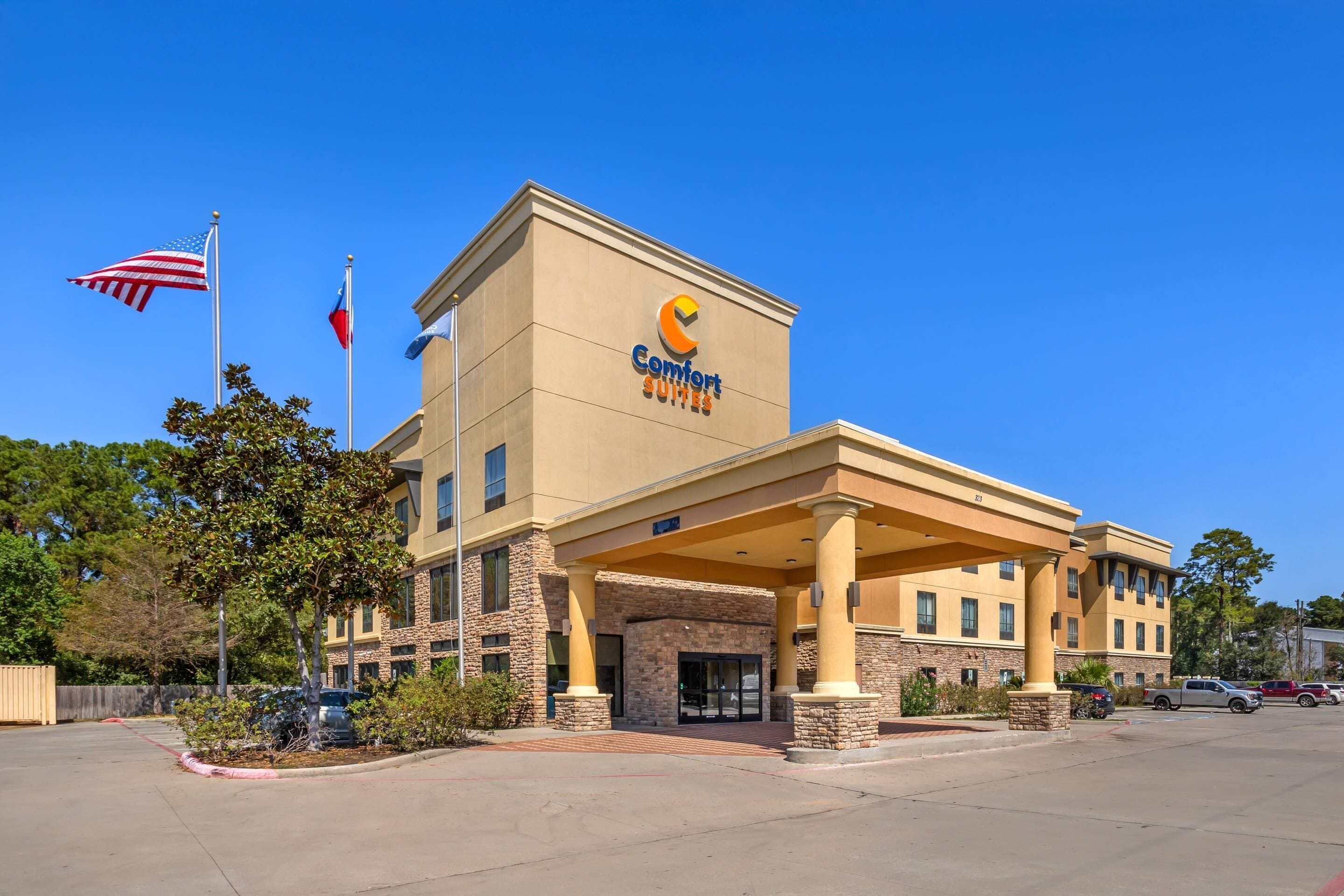 Un hotel Comfort Suites con fachada color crema, banderas estadounidenses y entrada cubierta.