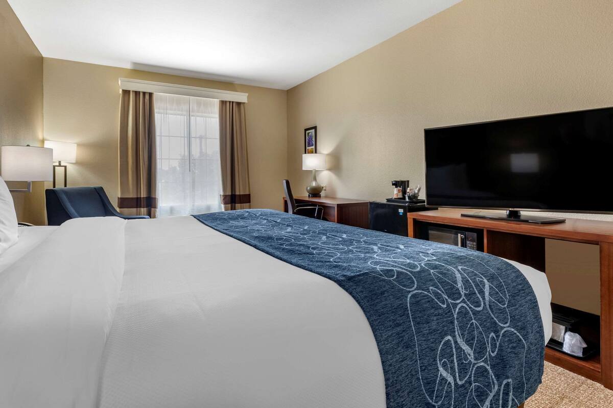 A hotel room with a large bed, a flat-screen TV, a desk, and a chair.