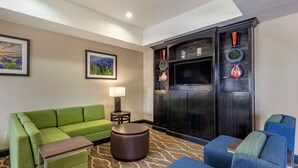 A hotel room with a green sofa, blue armchairs, a small round table, and a decorative cabinet with vases. - Comfort Inn & Suites Paris (Paris)