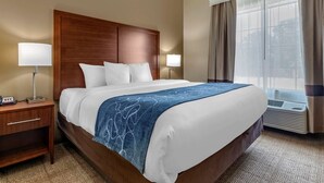 A hotel room with a large bed, two bedside tables, a nightstand, a window with curtains, and an air conditioning unit. - Comfort Inn & Suites Paris (Paris)
