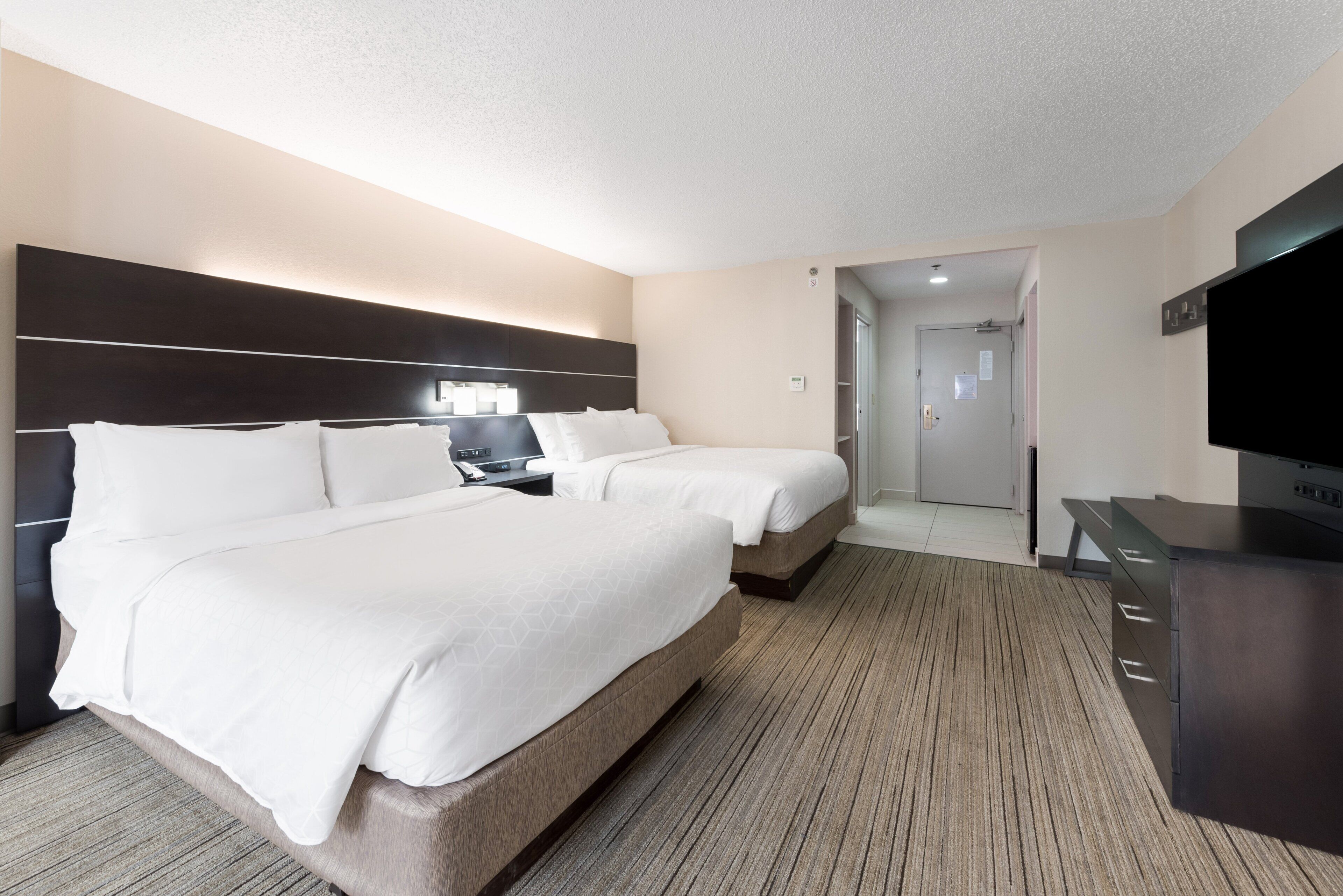 Habitación de hotel con dos camas, un escritorio con lámpara, televisión y puerta que da a un baño.