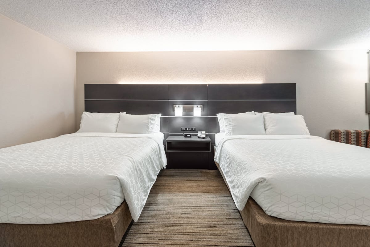 Une chambre d’hôtel avec deux lits, une table de chevet, une lampe fixée au mur et un plancher en bois.