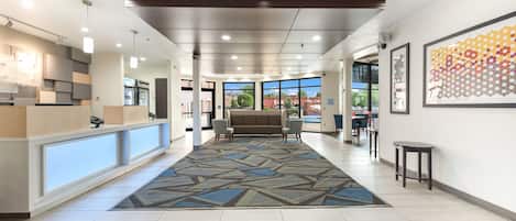 A hotel lobby with a reception desk, seating area, and large windows offering a view of the outside.