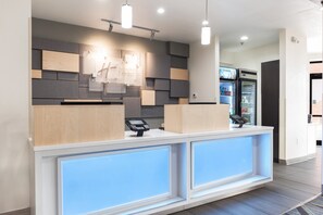 A hotel reception desk with a modern design, a digital payment terminal, and a refrigerator stocked with beverages.