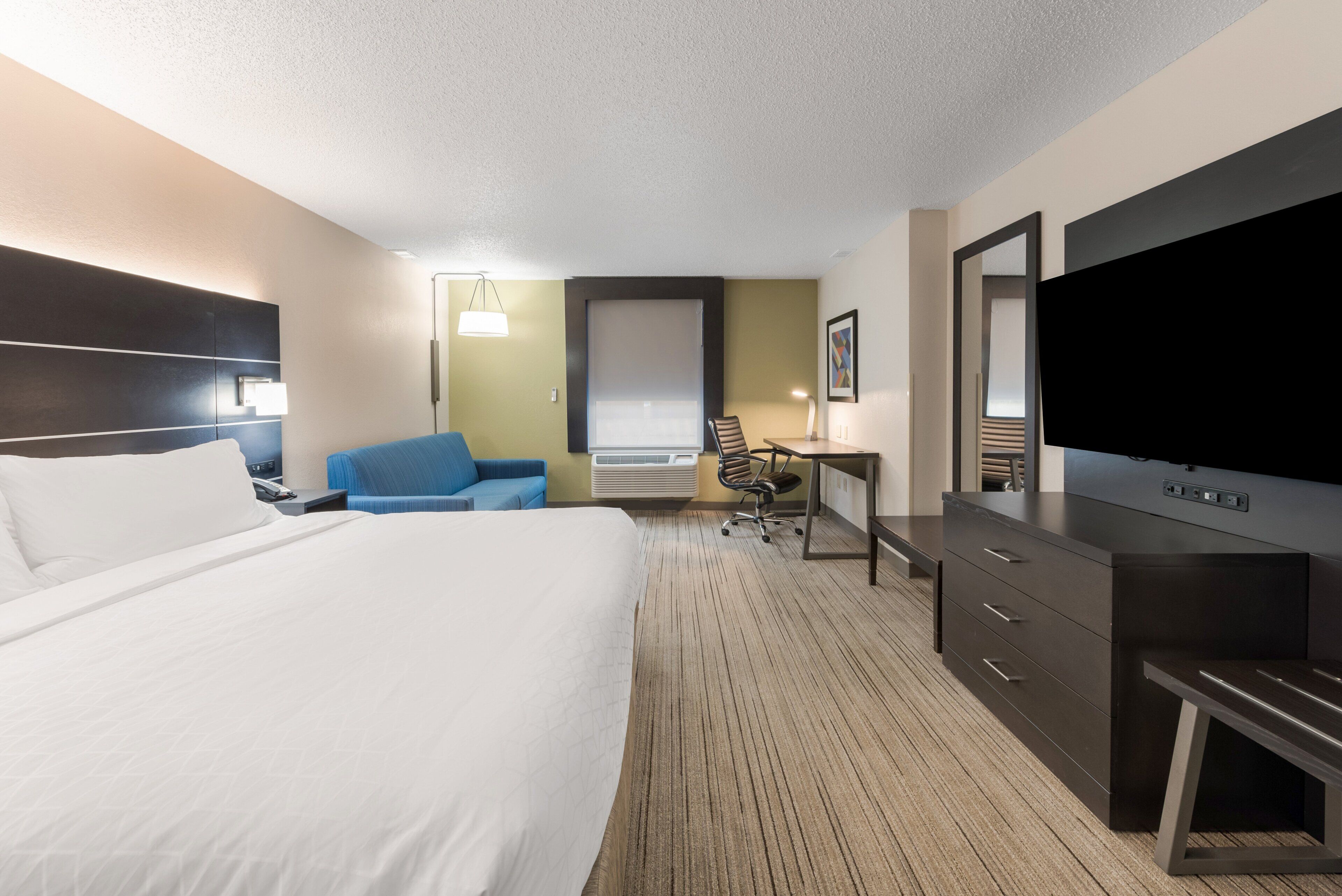 Quarto de hotel com uma cama grande, escrivaninha, cadeira, televisão e guarda-roupa.
