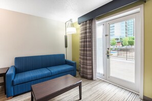 Habitación de hotel con sofá azul, una mesita, una lámpara y un ventanal corredero que da a un espacio exterior.